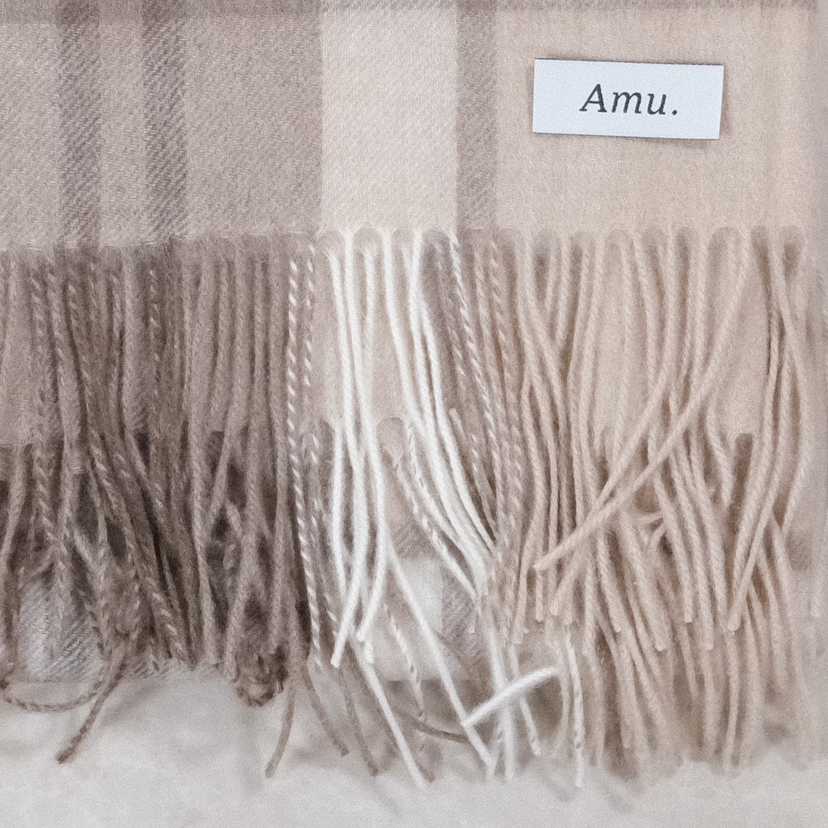 ラインチェックのカシミヤ生地とフリンジ、Amu.の織りネームの接写