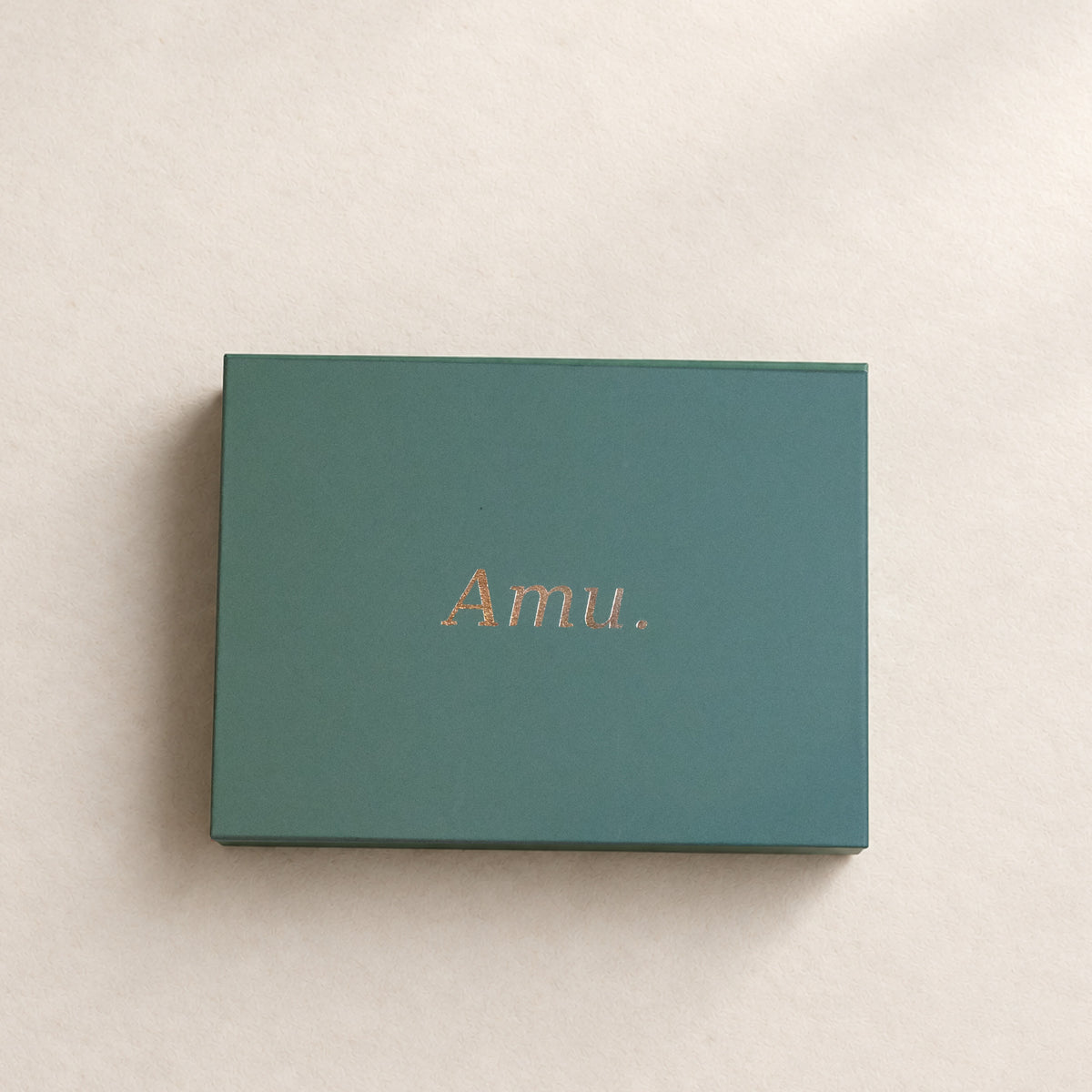 Amu.の深緑の無料ギフトボックス。蓋にゴールドのロゴ